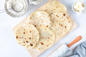 Homemade wheat tortillas, pita bread, tortilla, pita with ingredients for cooking on a white table. Top view. Vertical
